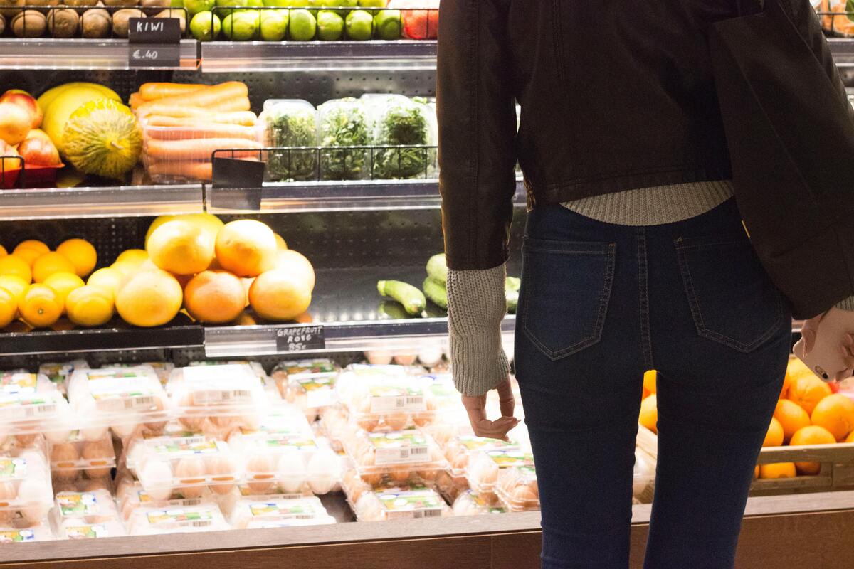 Mulher parada perto de uma prateleira de frutas no supermercado. 