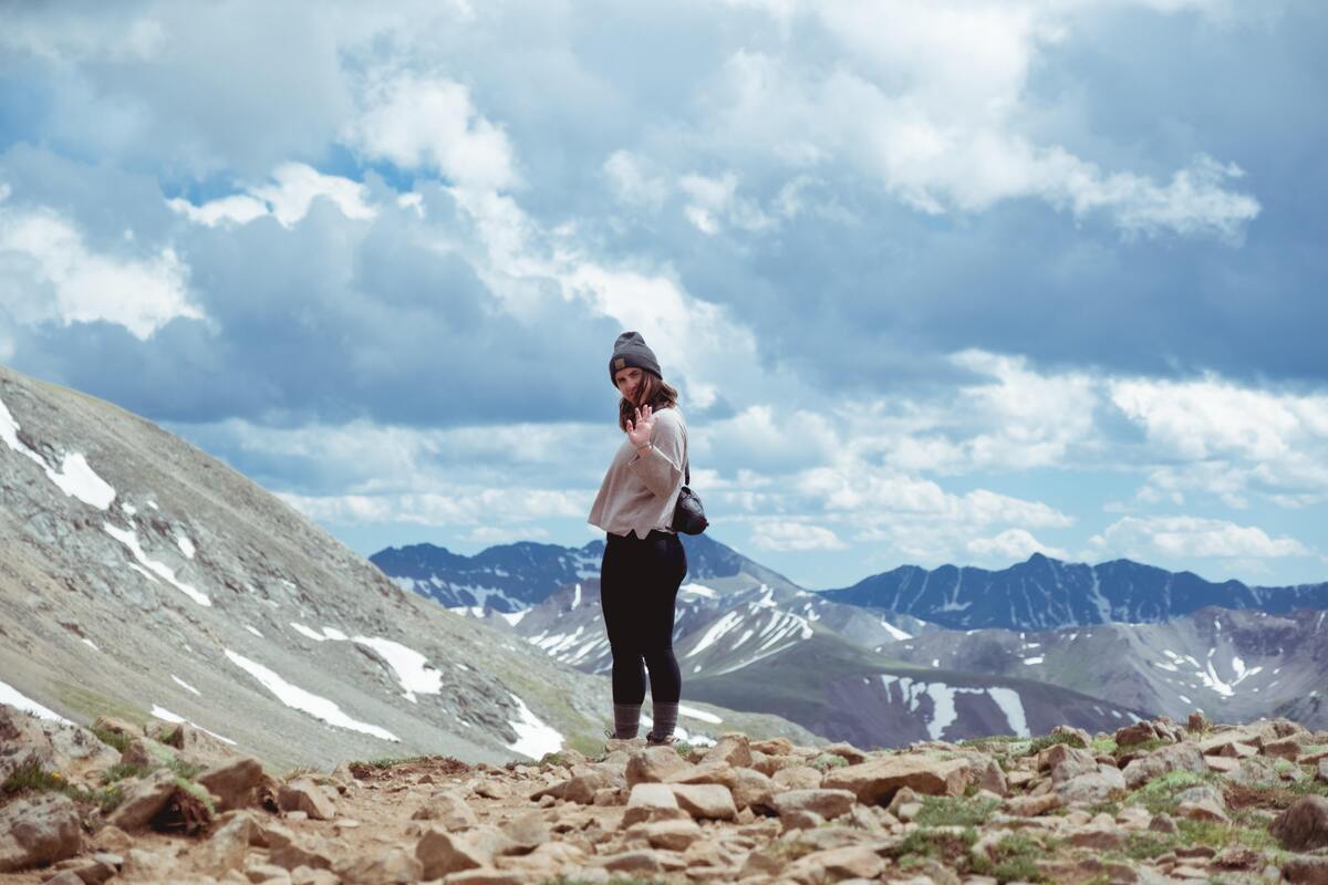 Mulher no topo de uma montanha, acenando para a câmera. 
