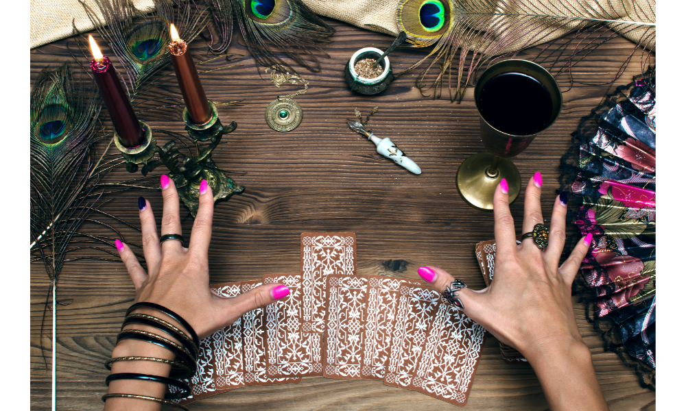 Mãos femininas sobre uma mesa com cartas de tarot e outros objetos esotéricos