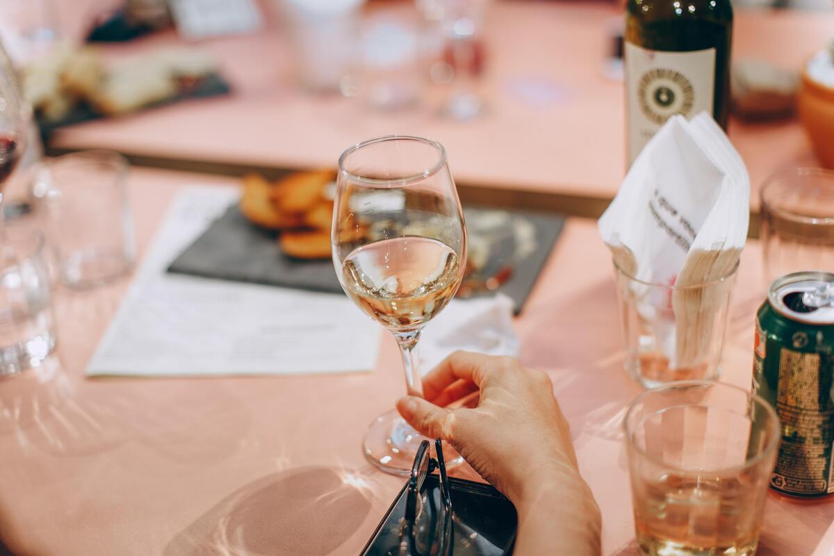 Uma mão segurando uma taça com vinho em cima de uma mesa