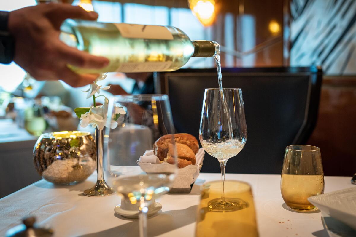 Uma mão derrubando vinho em uma taça sobre a mesa