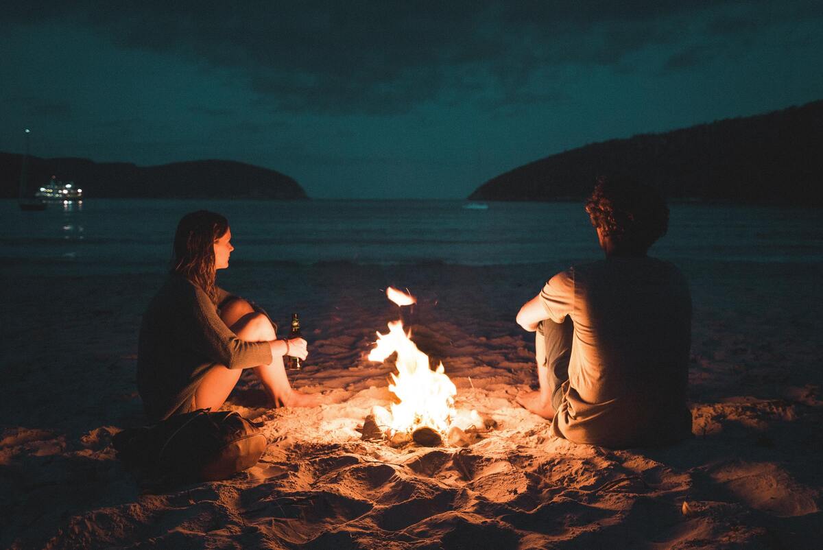 Um casal sentado em volta de uma fogueira. 