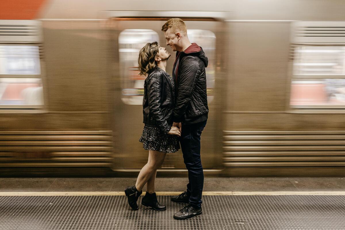 Casal se beijando na frente de um trem em movimento.