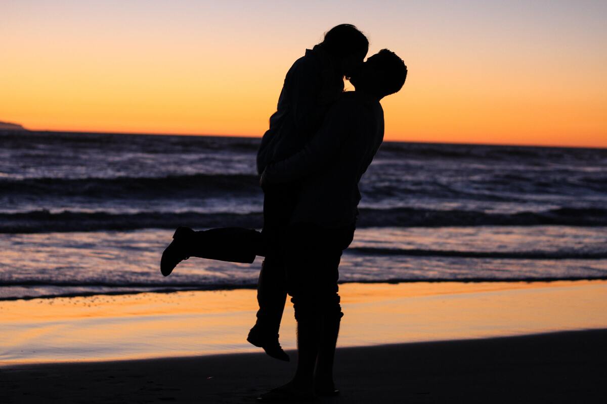 Homem levantando mulher enquanto se beijam na praia.