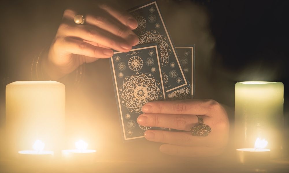 mulher segurando cartas de tarot numa mesa com velas