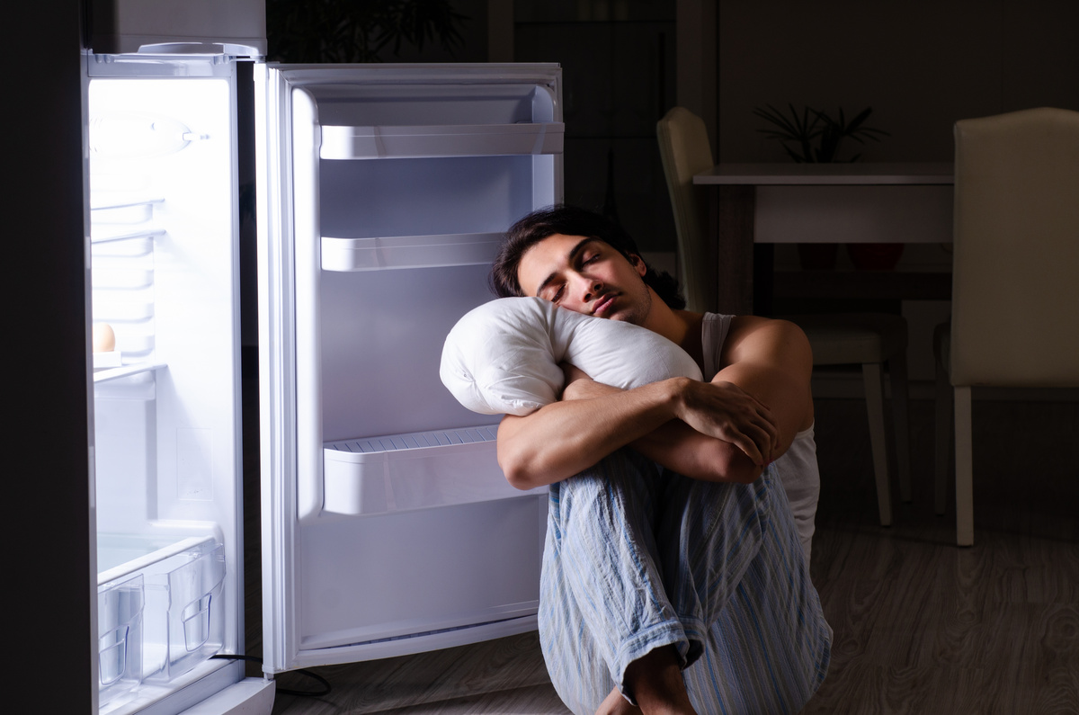 Homem dormindo encostado na porta aberta de um congelador
