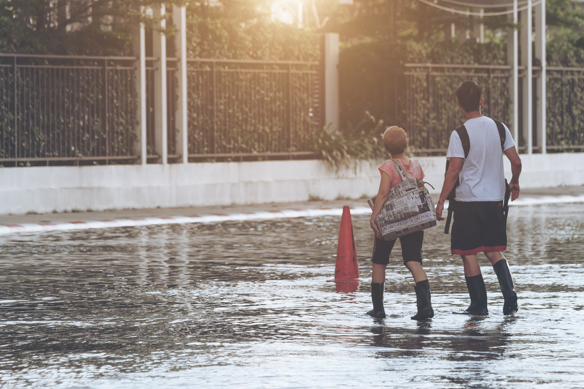 Um homem e uma mulher atravessando rua inundada por água