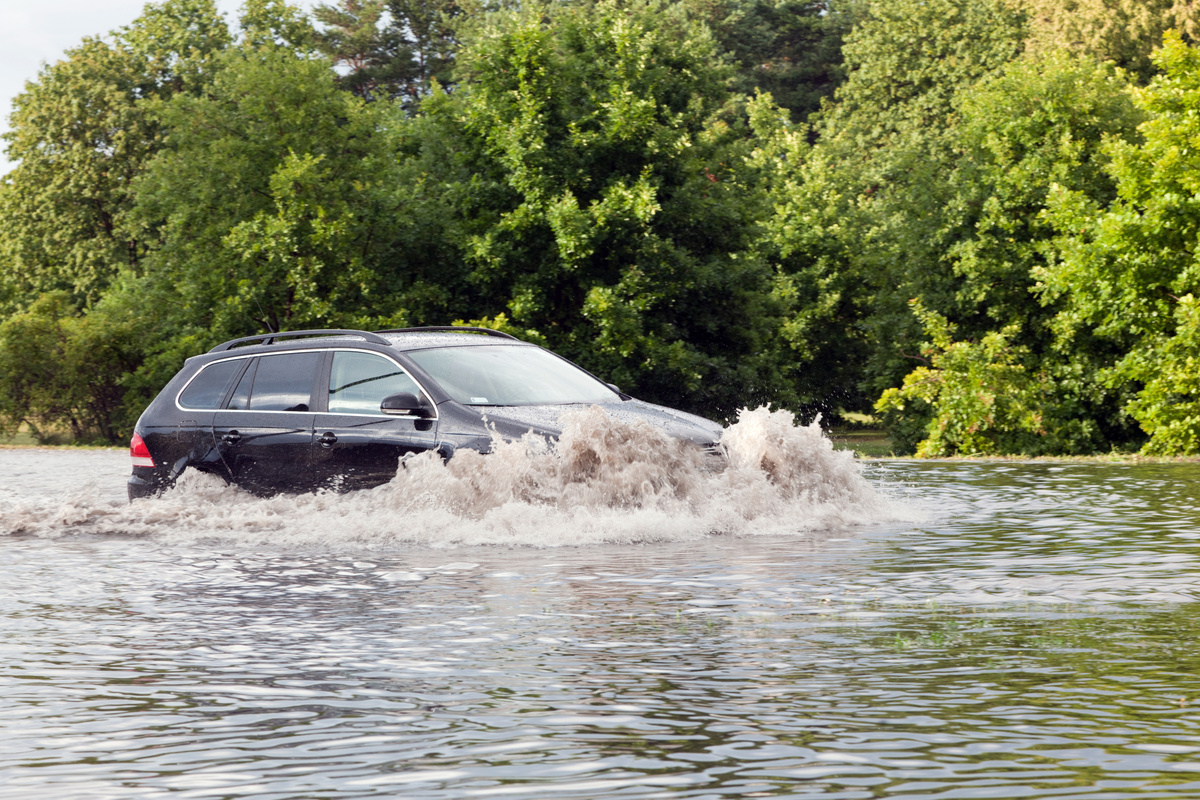 Carro atravessando rua inundada por água