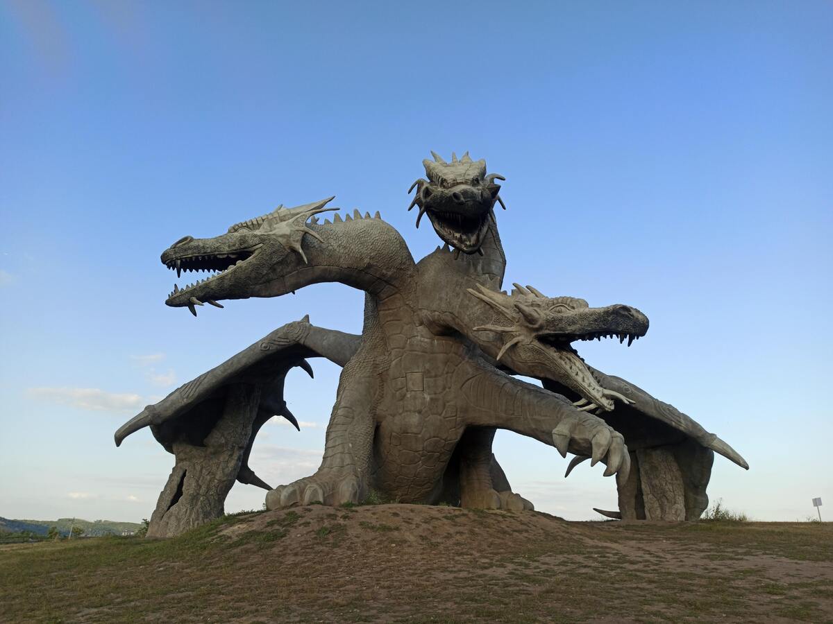 Estátua de um dragão de três cabeças em um campo gramado.