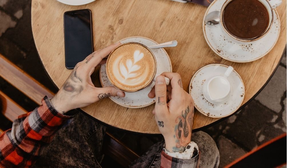 Mãos tatuadas de homem segurando xícara branca de café