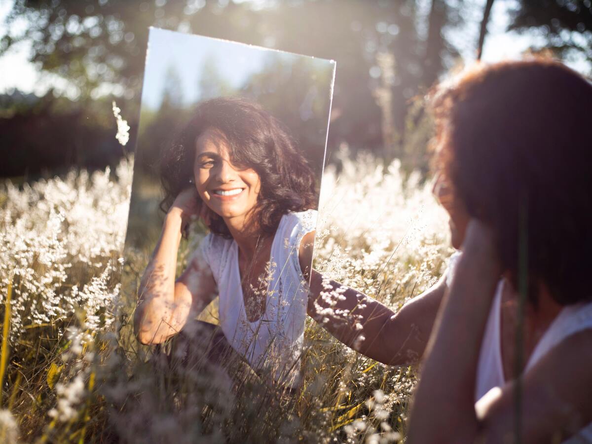 Mulher sorrindo para si mesma no espelho.