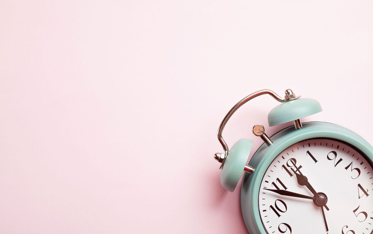 Relógio despertador azul em fundo rosa.