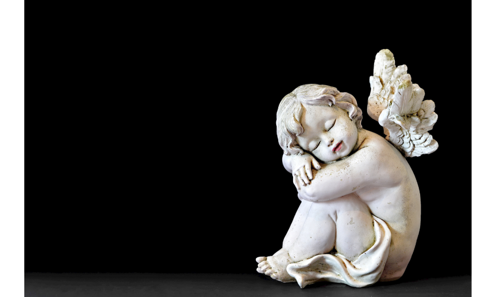Foto de uma escultura de anjo sentada e com um fundo preto.
