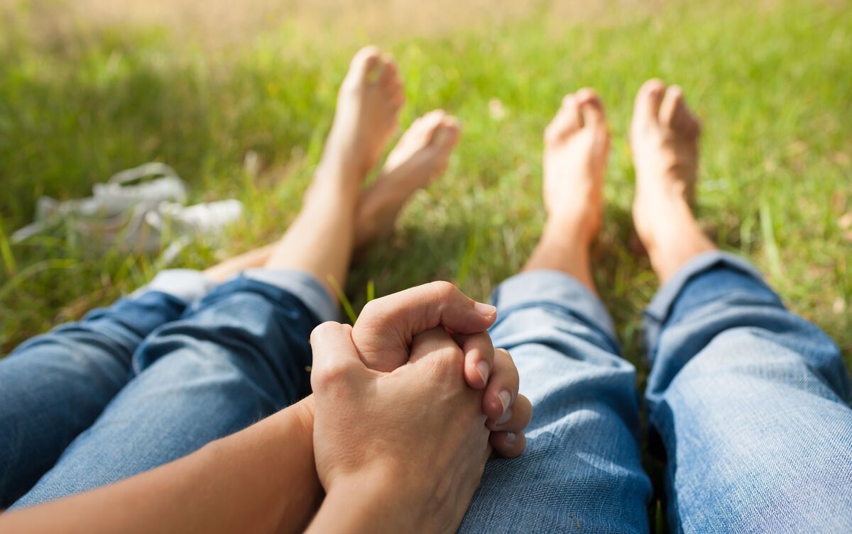 Casal sentado em grama de mãos dadas.
