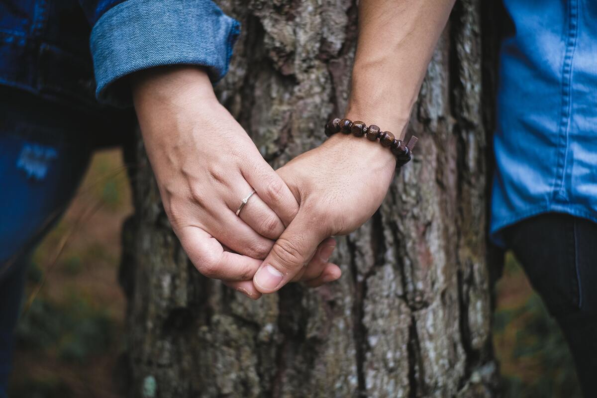 Casal dando a mão, tronco de árvore ao fundo.