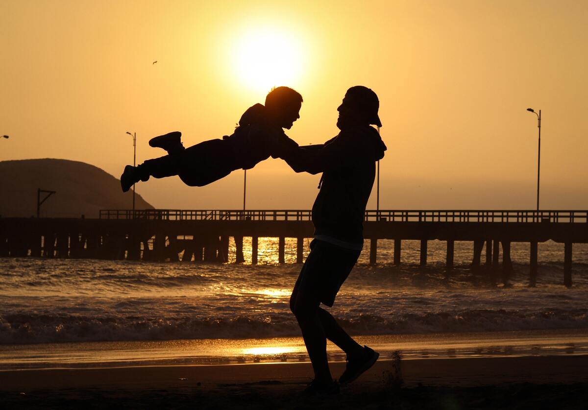 Homem girando uma criança no ar em uma praia.