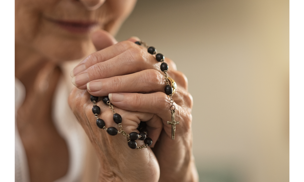 Mãos unidas em oração junto de um rosário.