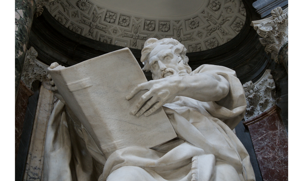 Escultura de São Mateus sentado com um livro aberto nas mãos.