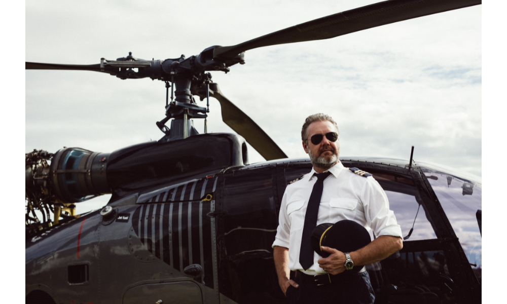 Piloto com óculos escuros em frente a um helicóptero.