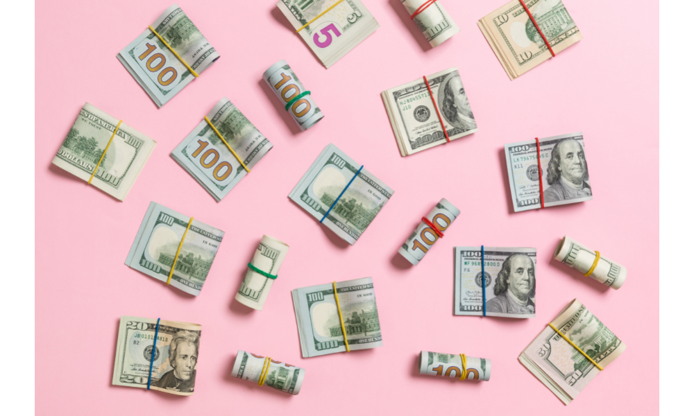 Notas de dinheiro espalhadas por uma mesa rosa.