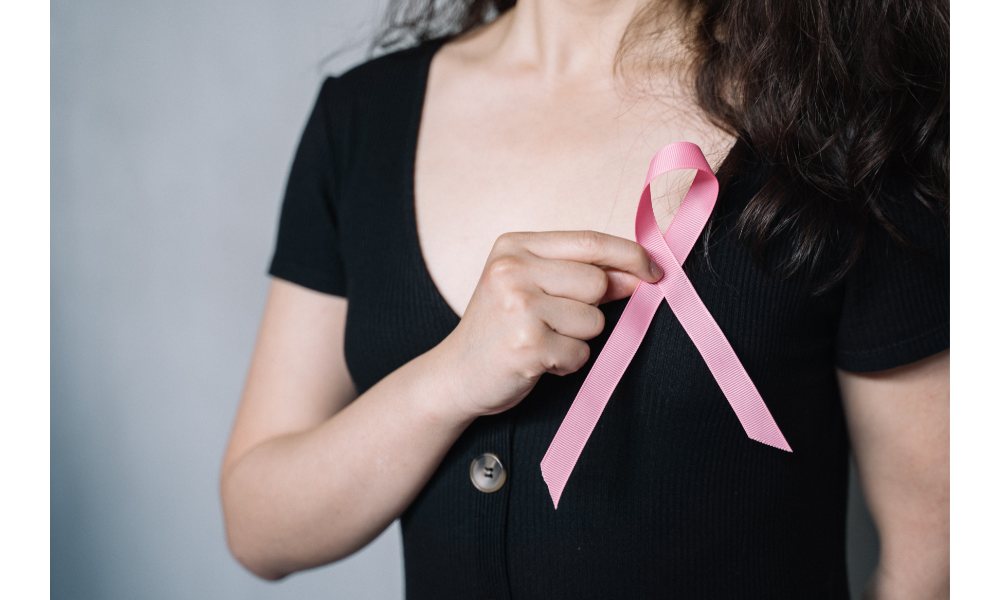 Tórax de uma mulher com uma fita rosa em frente ao seio, símbolo da prevenção do câncer de mama.