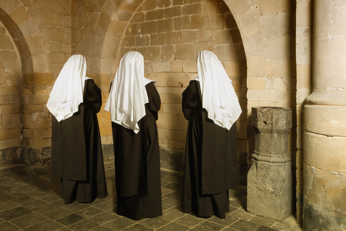 Três freiras de costas olhando para parede em igreja