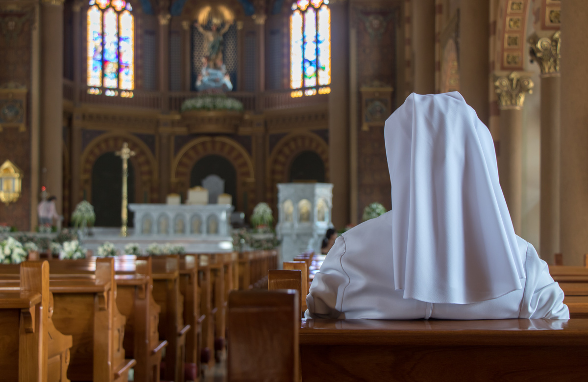 Freira de roupa branca sentada em banco de igreja