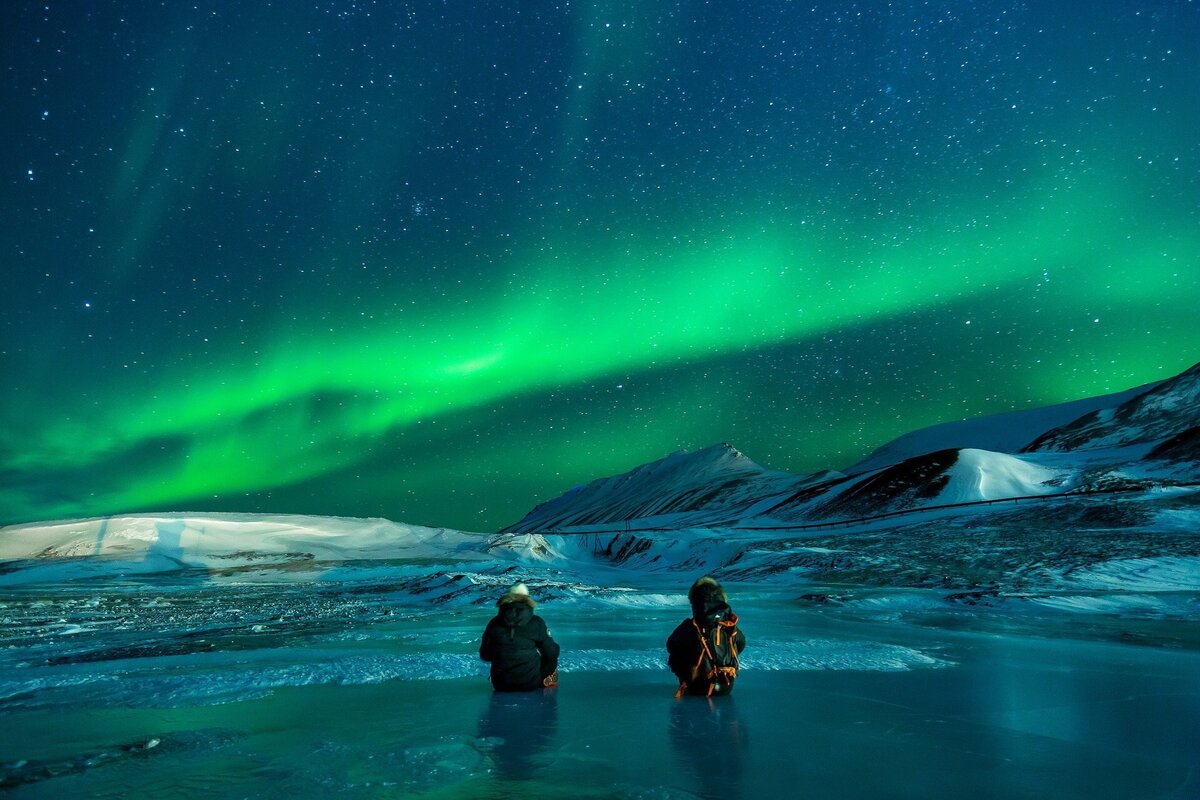 Pessoas sentadas no gelo olhando o céu