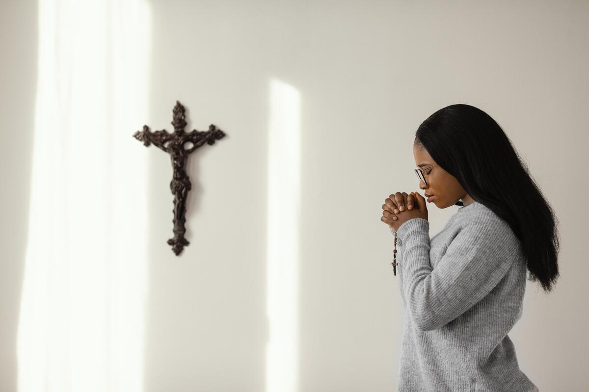 Mulher rezando com terço em frente a cruz