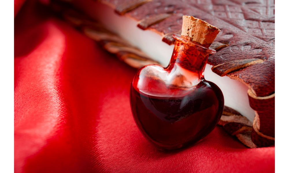 Poção do amor - vidro em formato de coração com líquido vermelho apoiado em um tecido vermelho.