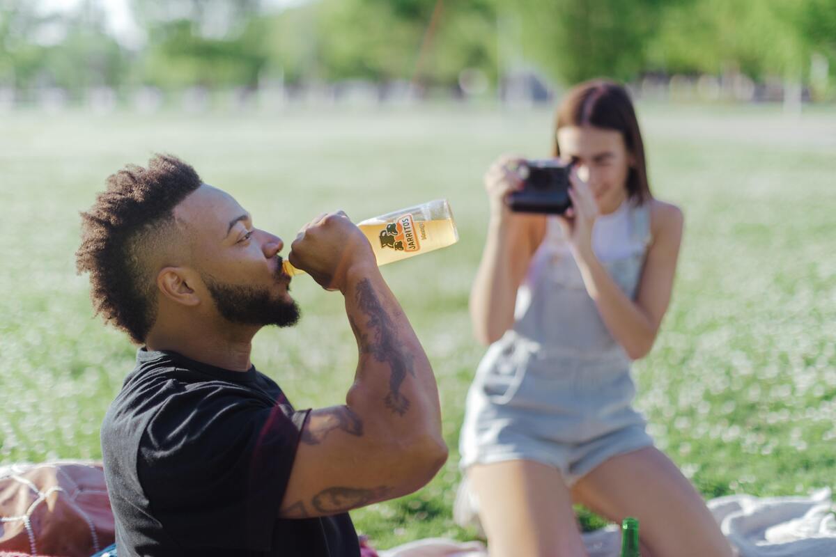 Mulher tirando foto de um homem bebendo de uma garrafa. 
