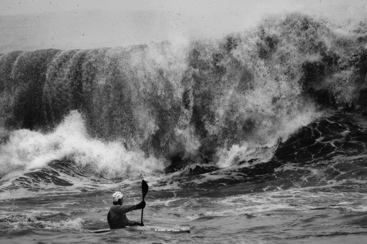 Homem em canoa próximo a grande onda