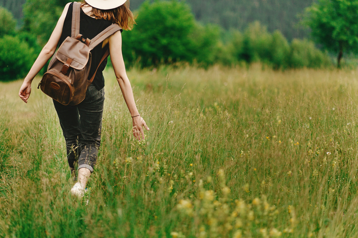 Garota com mochila nas costas caminhando em campo com plantação alta.