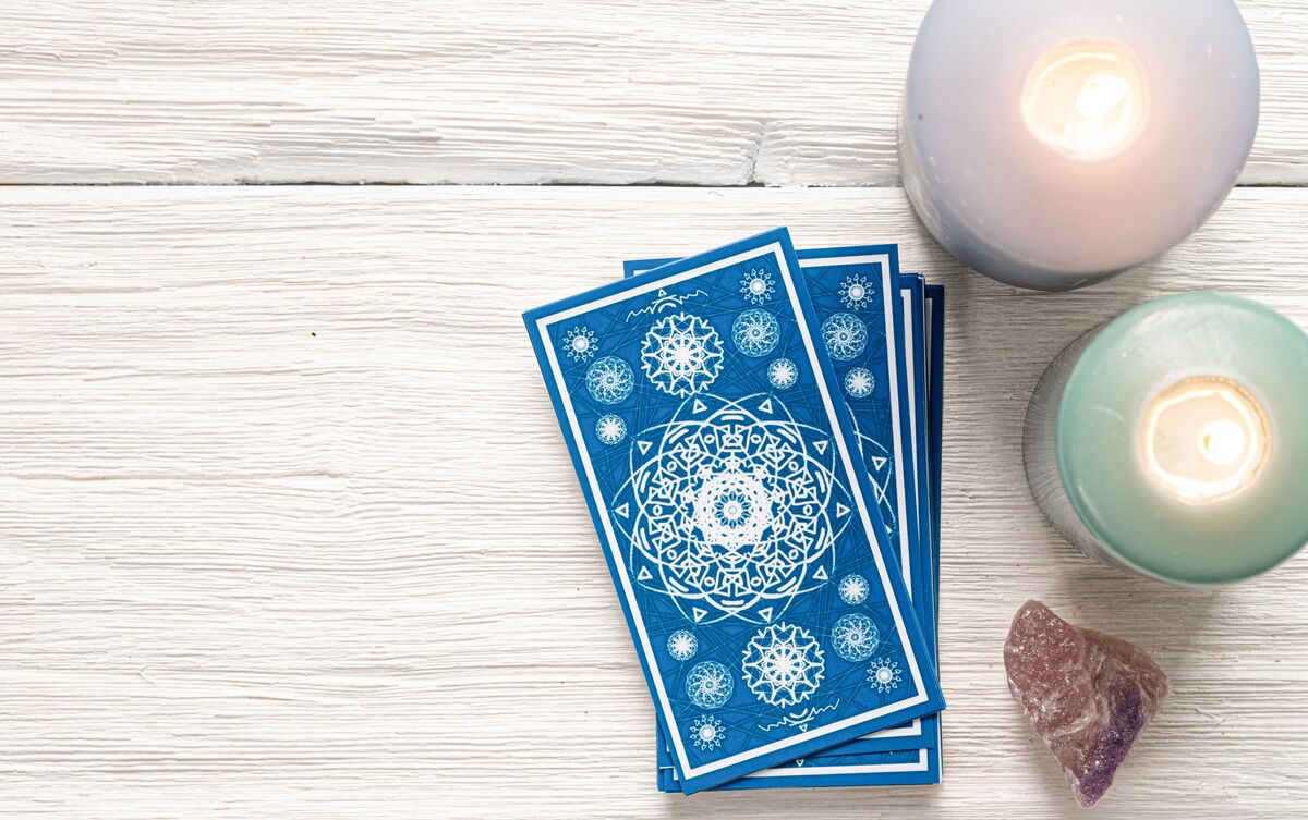 Cartas de Tarot empilhadas em mesa de madeira com velas ao lado.