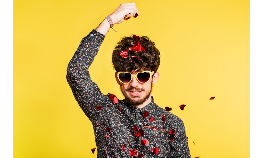 Homem com óculos amarelo jogando pétalas de rosas sobre sua cabeça.