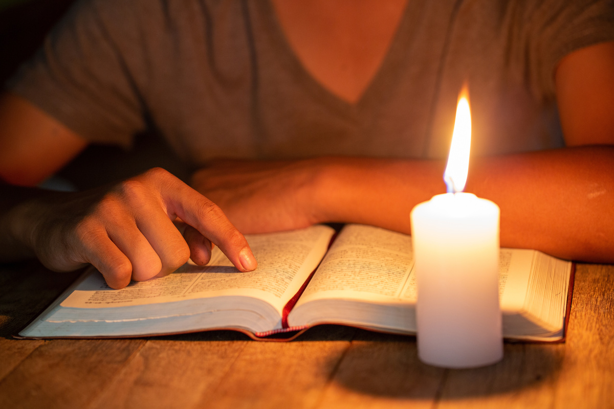 uma mulher apontando em um livro e uma vela acesa 