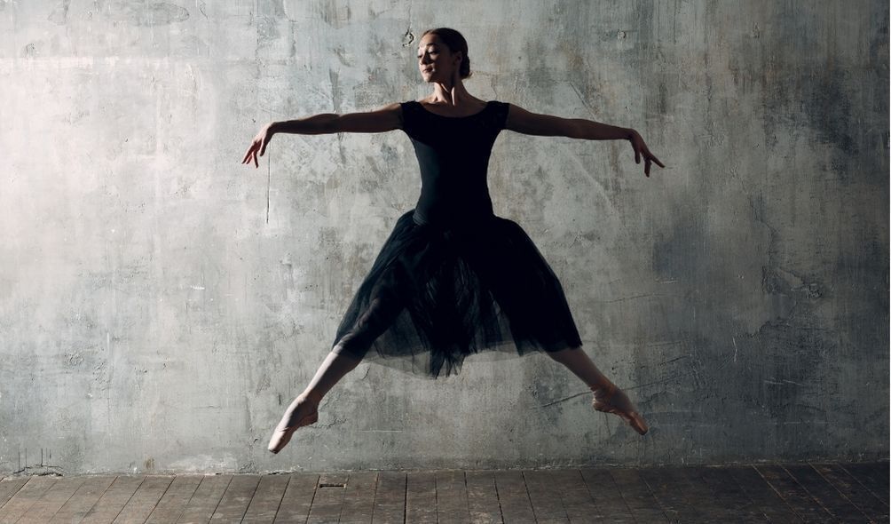 Bailarina com vestido preto fazendo passo de ballet