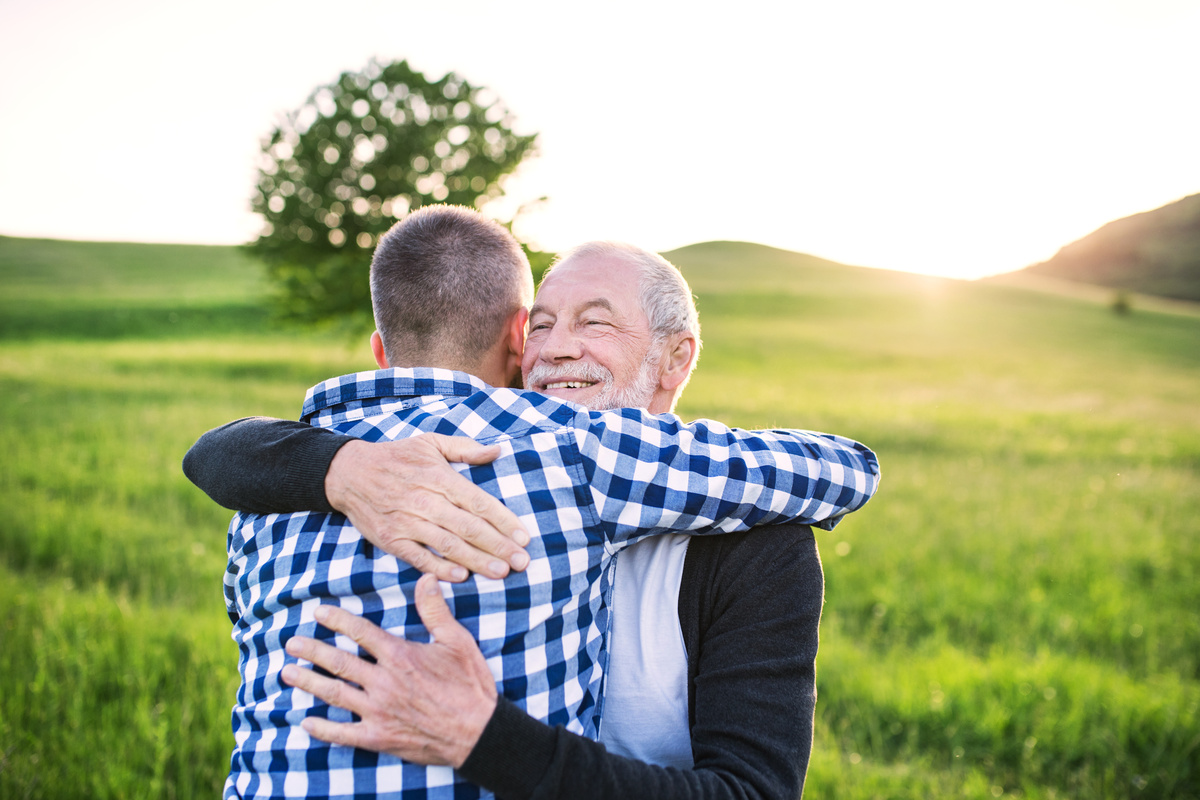 Homem abraçando seu pai num campo verde