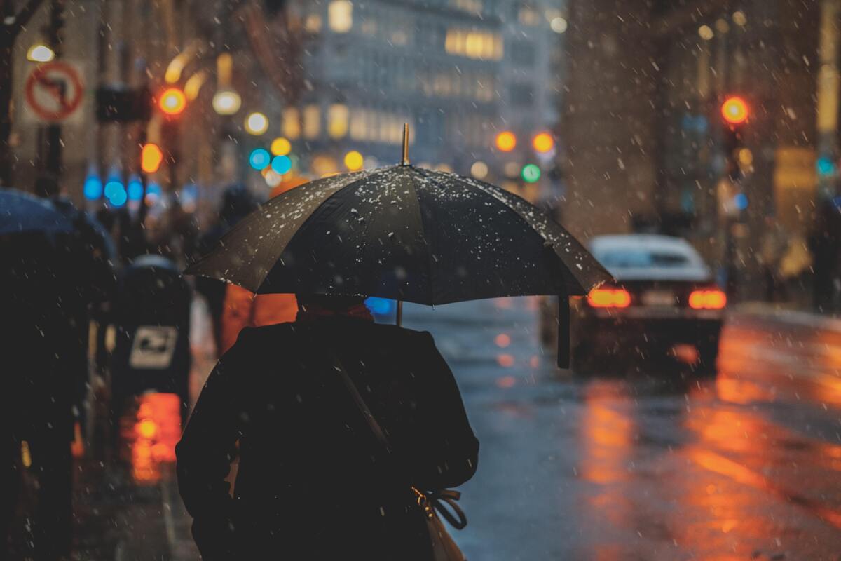 Mulher de costas segurando um guarda-chuva na rua.