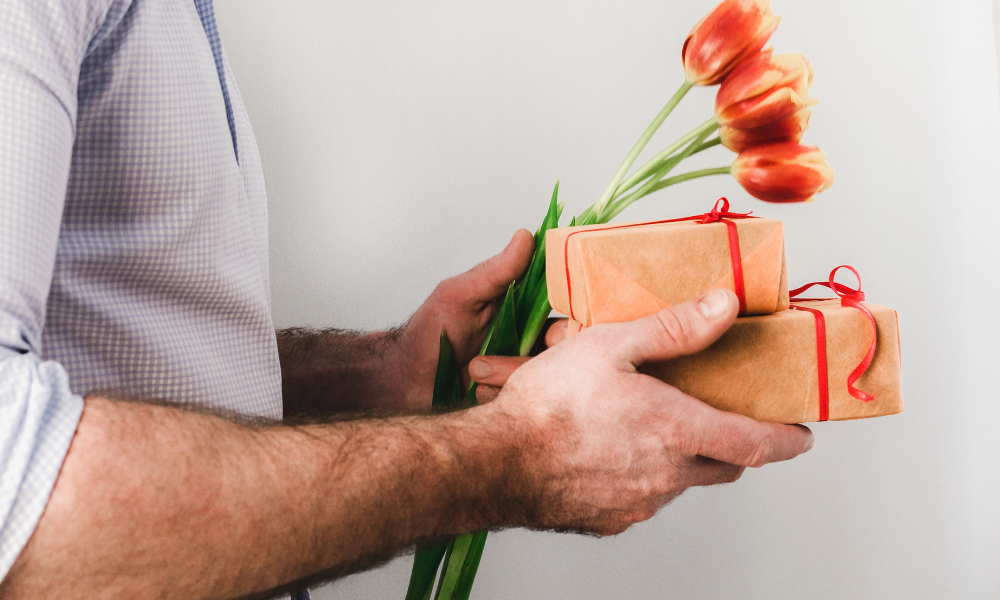 Homem segurando presentes e flores nas mãos.