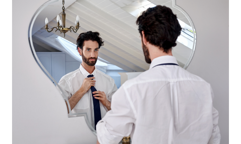 Homem arrumando sua gravata em frente a um espelho.