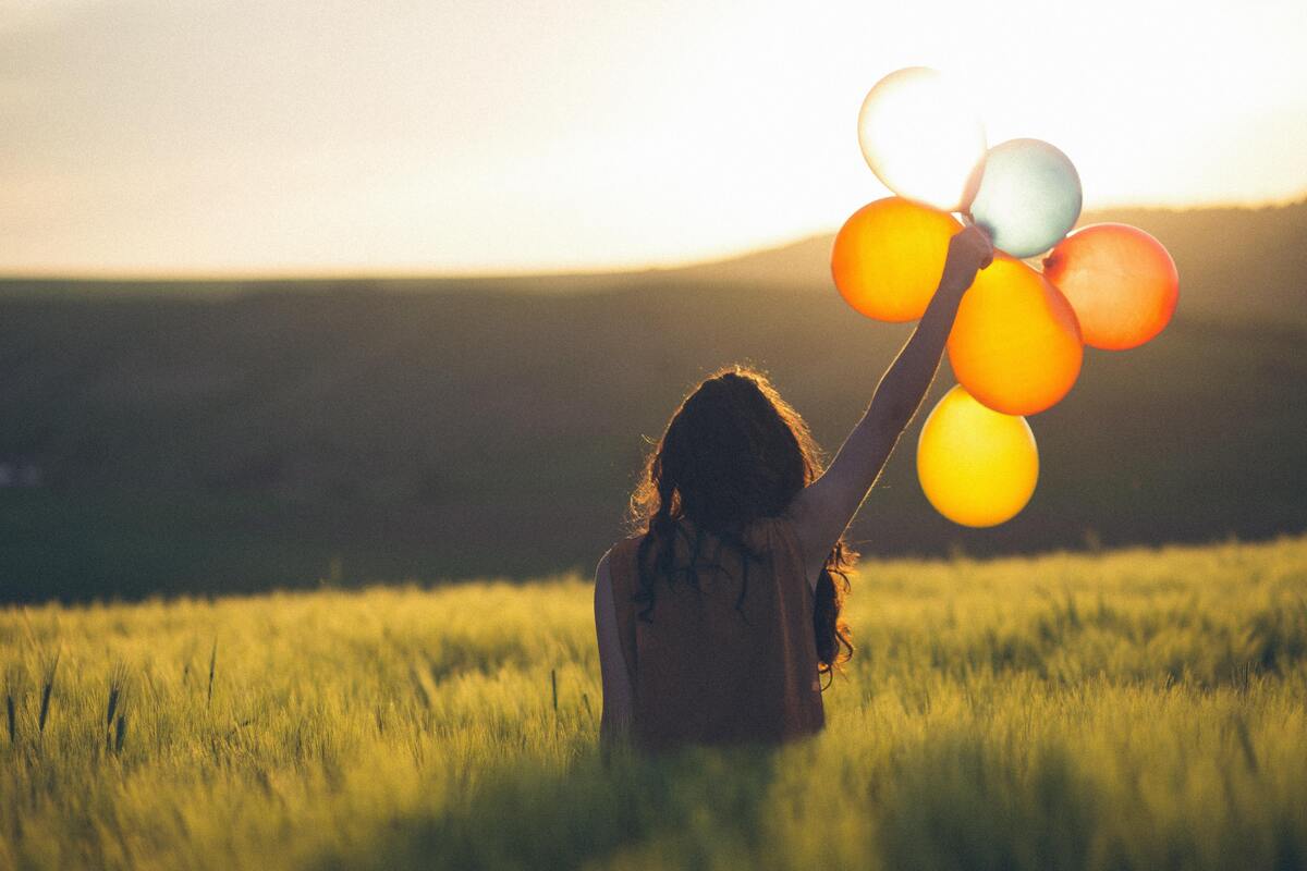 Mulher segurando balões em um campo gramado.