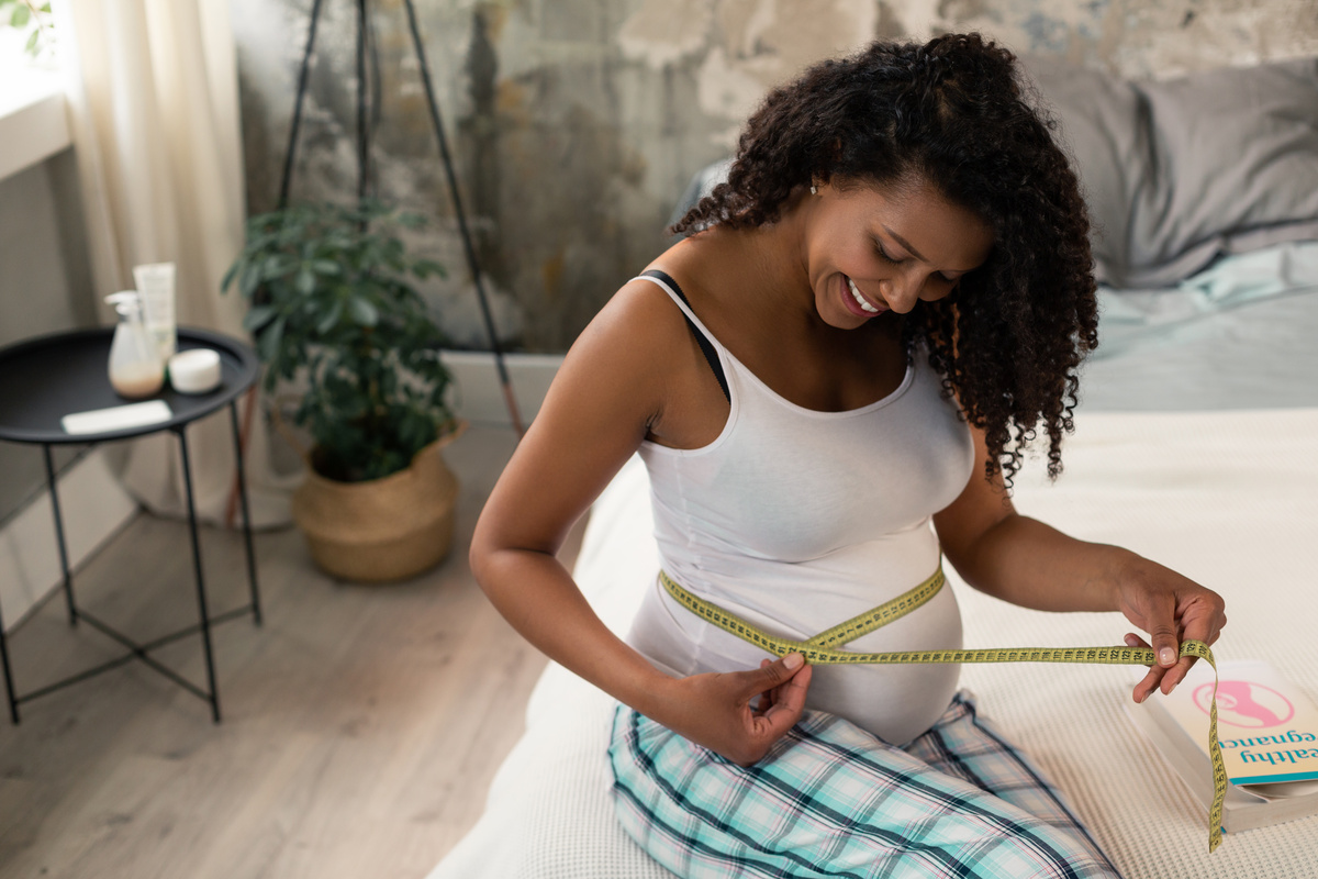  Mulher grávida medindo sua barriga com fita métrica