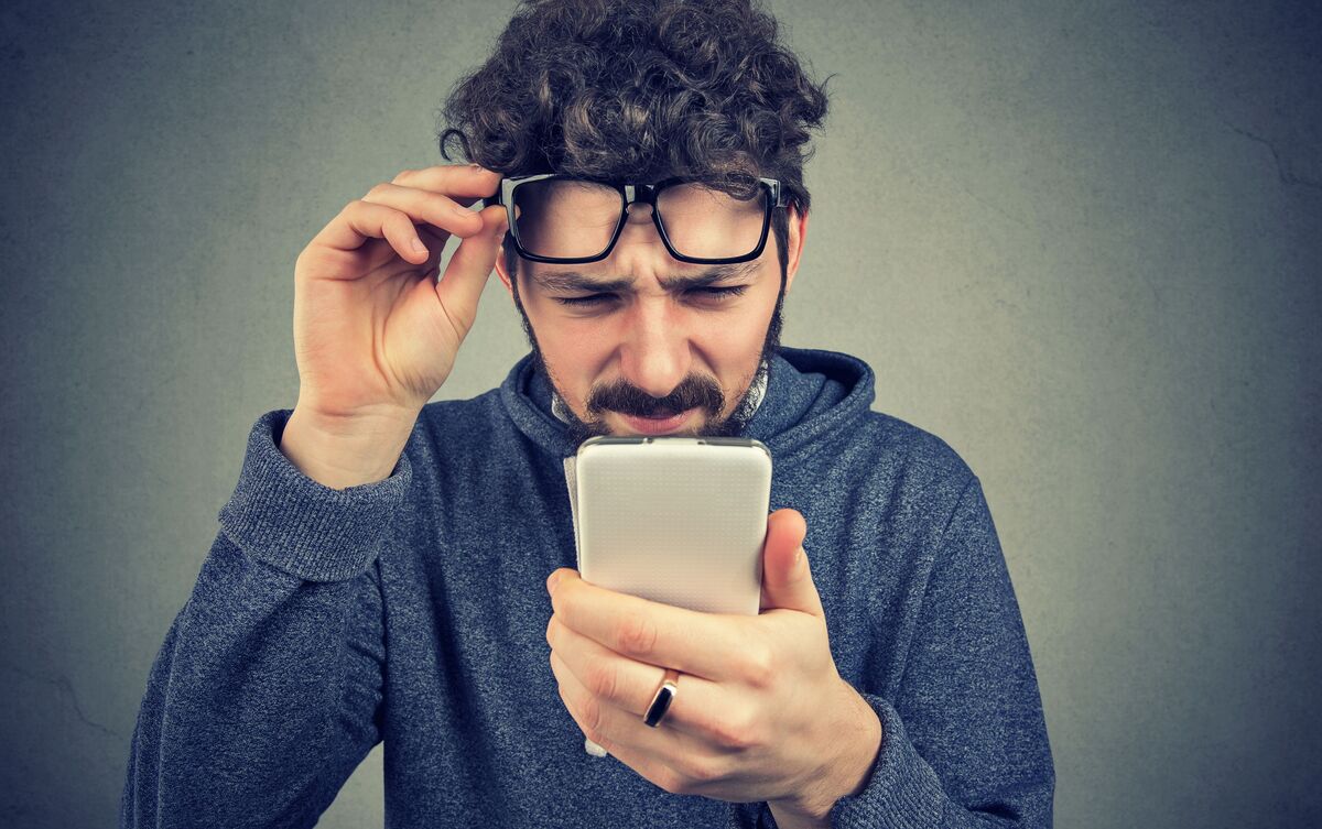 Homem de óculos tentando ler conteúdo de seu celular.