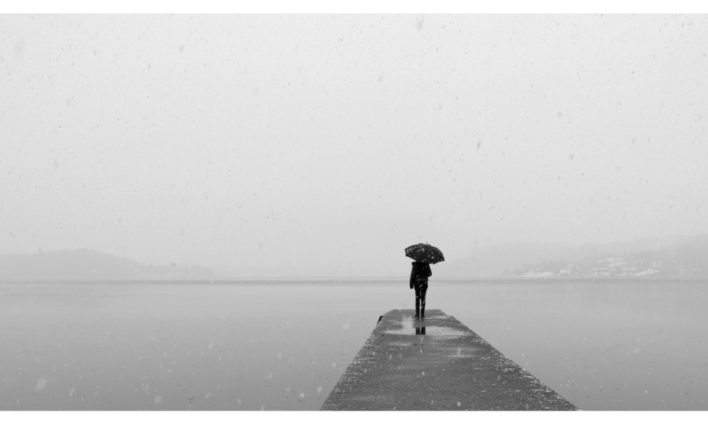 Pessoa solitária com guarda-chuva, ambiente com neblina.