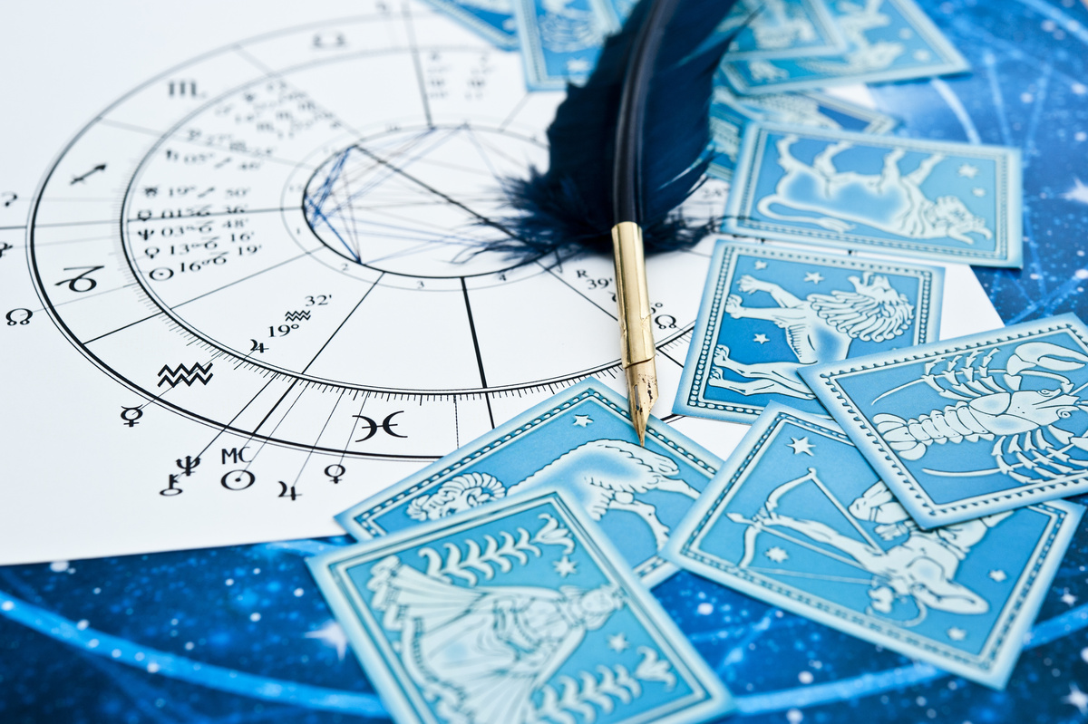 O mapa de interpretação do trânsito astrológico, com uma caneta de pena em cima, e rodeado de cartas com os símbolos do zodíaco.