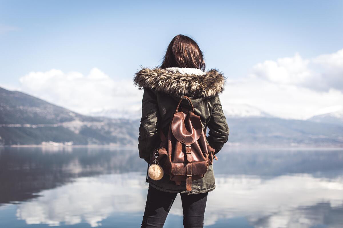 Menina com mochila olhando uma paisagem. 