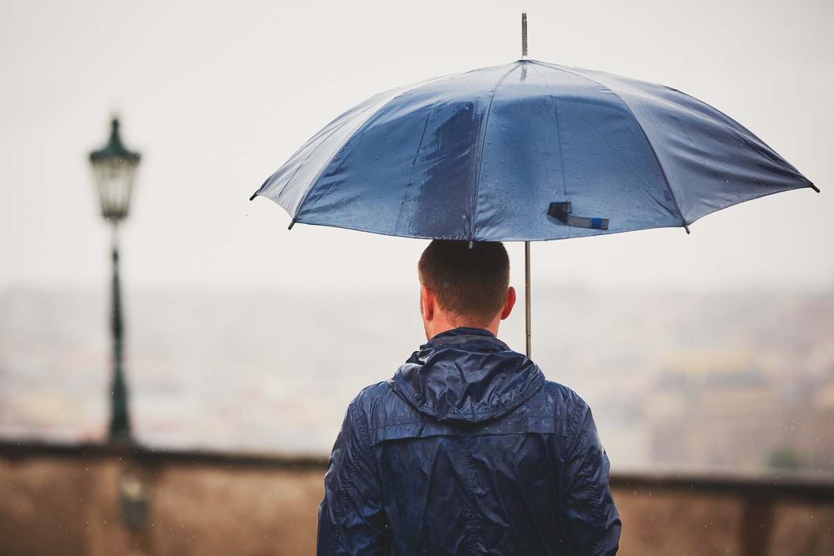 Homem segurando guarda-chuva azul na chuva