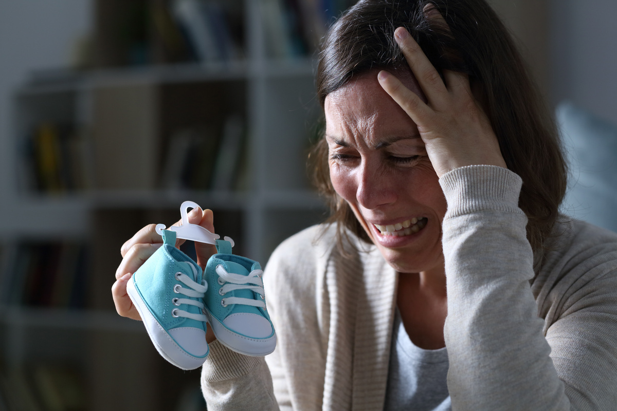 Mãe chorando com sapatinho de filho recém-nascido morto.