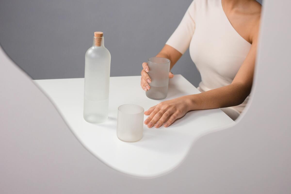 Reflexo de mulher tomando água em copo e garrafa fosca